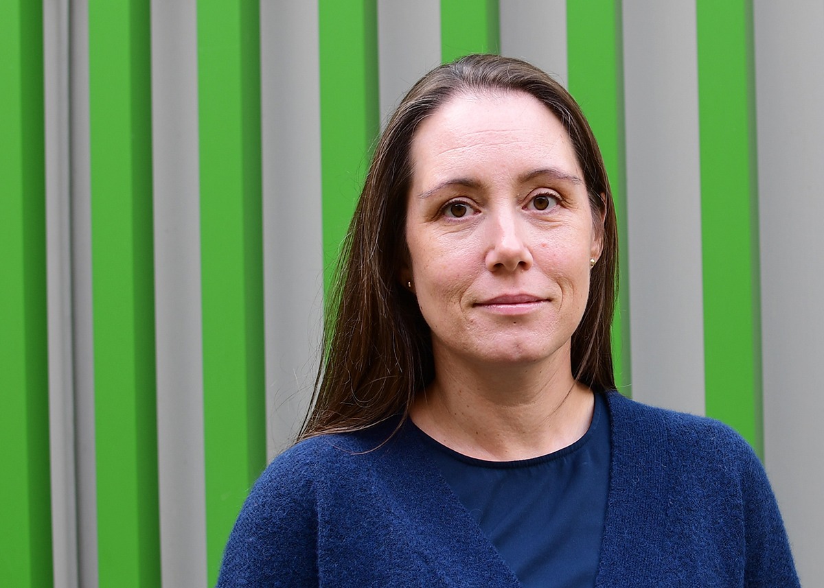 Frida Lind facing the camera, with green lines in the background at meetingplace Navet.