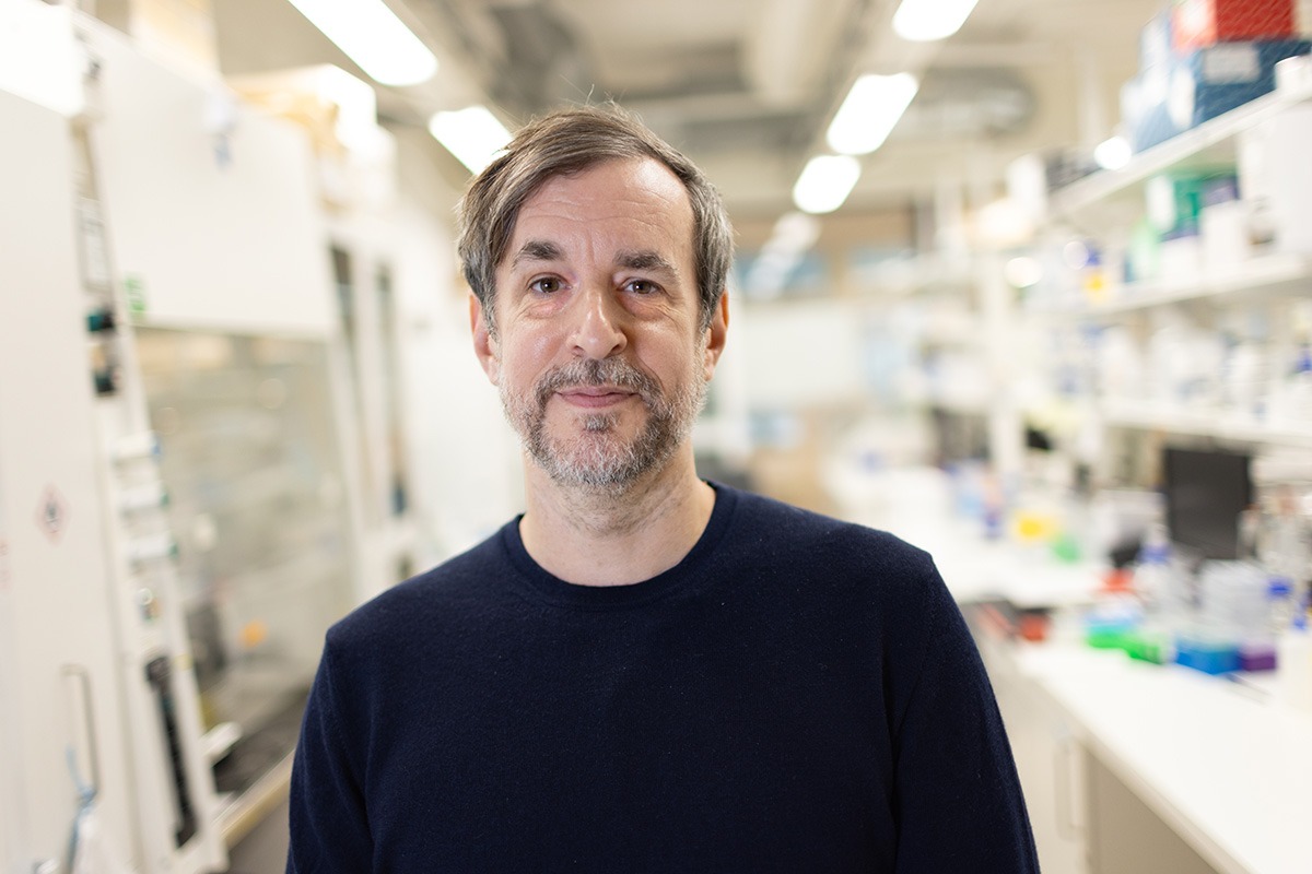 Marc Friedländer standing in a bright laboratory environment, with blurry lab equipment in the background.