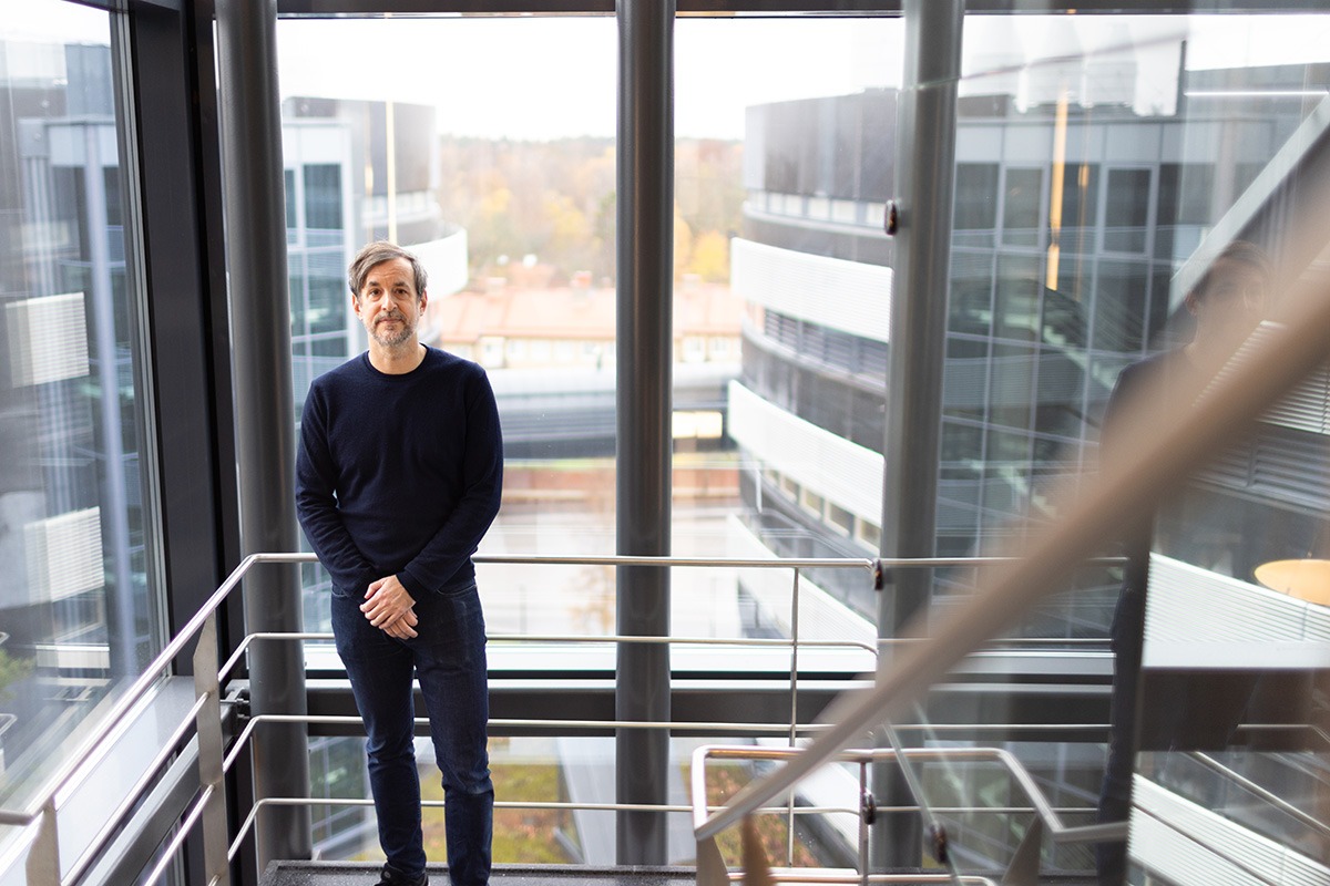 Marc Friedländer standing in the glass-covered staircase at SciLifeLab Campus Solna, with two of the three characteristic oval SciLifeLab buildings seen through the windows.