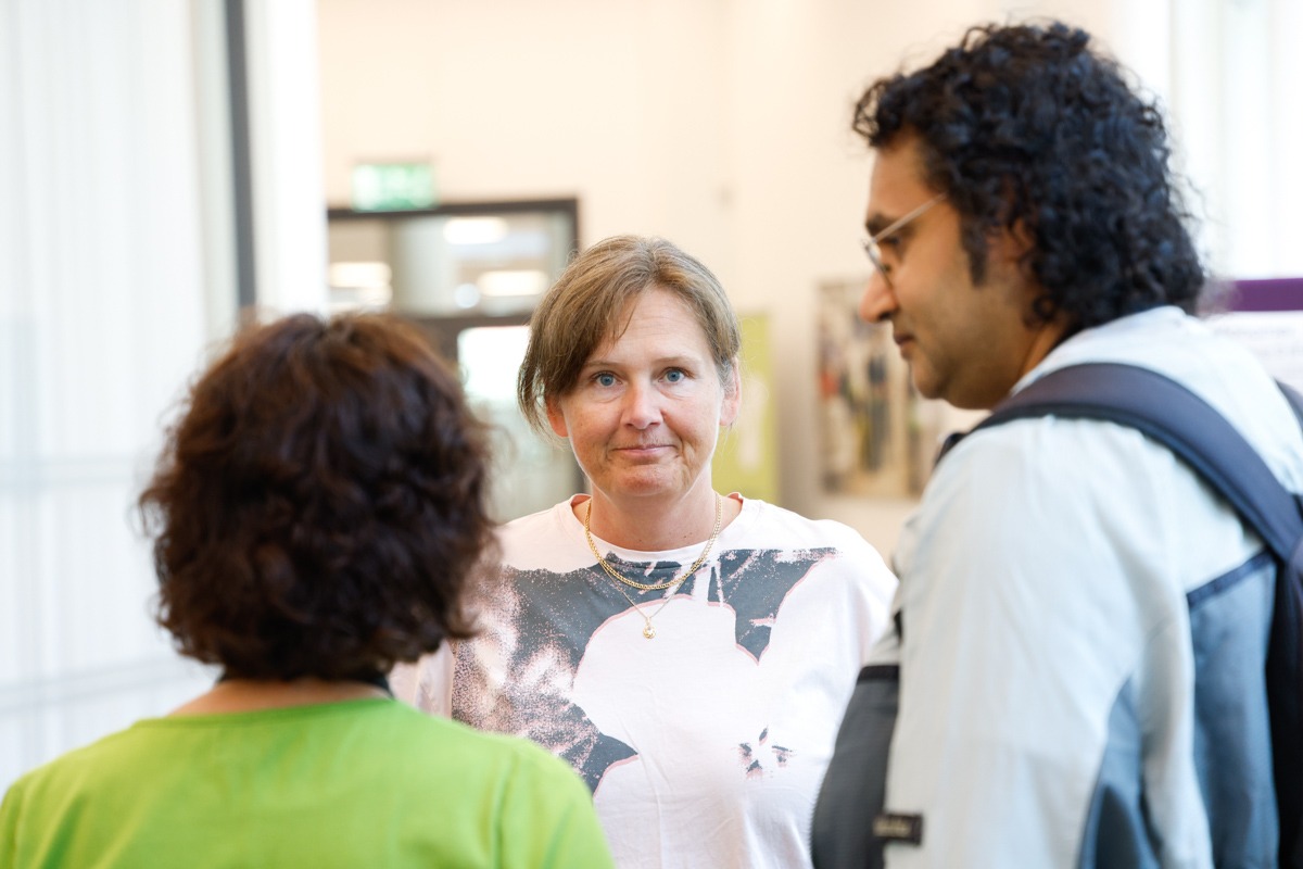 Cecilia Persson is standing at a slight distance and looks into the camera. In the foreground, two persons she is standing together with are out of focused due to shallow depth of field.