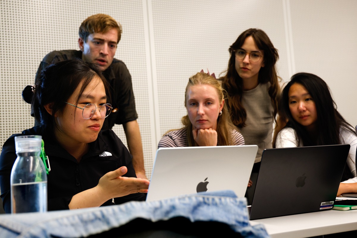 Five participants at the course sitting in front of one computer, with one person points at the computer and appears to explain something.