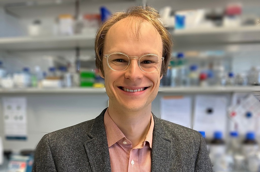 Florian Rosenberger looking into the camera, standing close to it, with blurry laboratory equipment in the background.